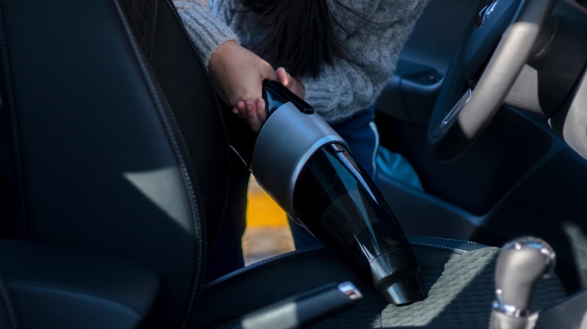 Osoba sprząta wnętrze samochodu przy użycu ręcznego odkurzacza, zdjęcie utrzymane w kolorach ciemnych i niebieskich