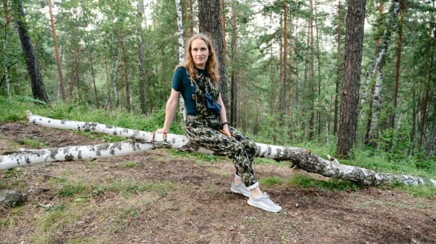 Kobieta o długich włosach siedzi w lesie na brzozie, na noga ma białe sneakersy