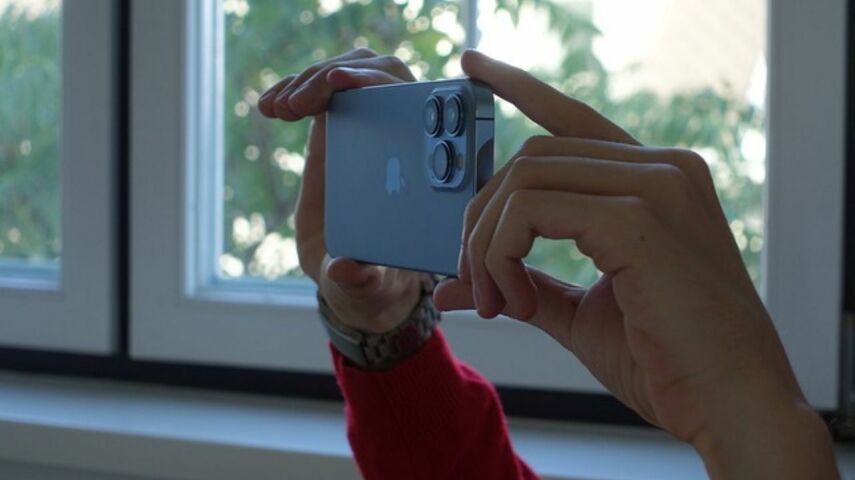 Na tle okna trzymany w dłoniach Iphone 13 pro w trakcie robienia zdjęcia