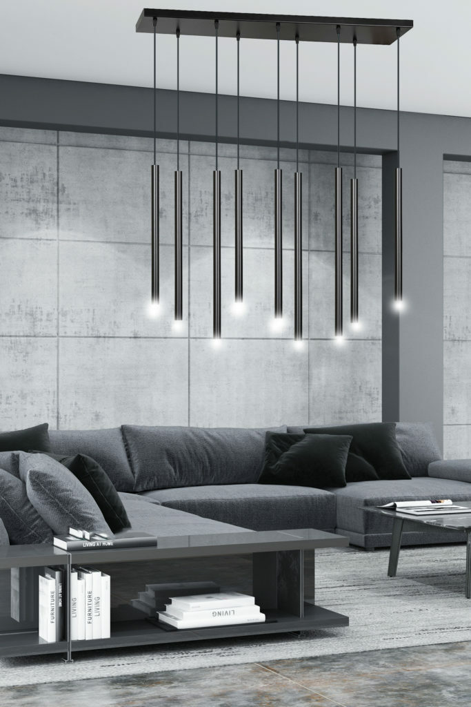 Długie, cieńkie wiszące lampy o nowoczesnej formie na tle betonowej ściany i szarej kanapy