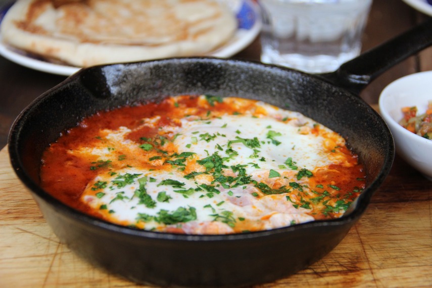 Jajka gotowane w pomidorach na stalowej patelni, posypane świeżym szczypiorkiempiorkiem