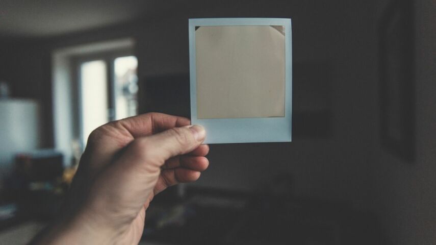 Dłoń trzymająca stare zdjęcie niczym z polaroidu na tle mieszkania