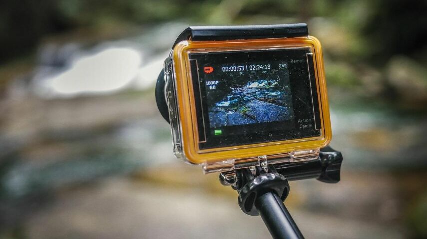 Żółta kamera sportowa na wysięgniku, widoczny ekran, całość na tle lasu