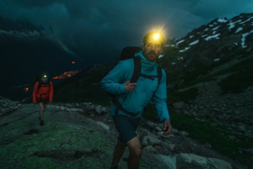 W ciemnych górach mężczyzna z czołówką na głowie w zaawansowanym sprzęcie sportowym Arcteryx