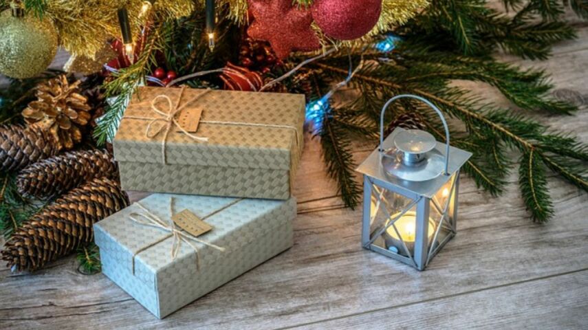 Na podłodze drewnianej pod choinką stoi lampion oraz zapakowane w ozdobny papier udane prezenty na święta