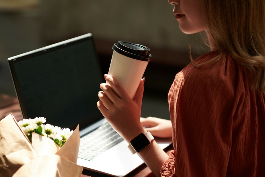 Młoda kobieta freelancer IT ptacuje na laptopie trzymając w ręku kawę