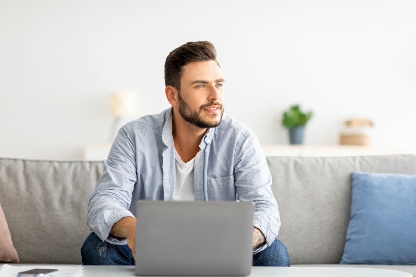 Mężczyzna freelancer IT pracuje na laptopie siedząc na sofie