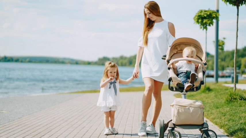 Kobieta z dzieckiem za rękę oraz dzieckiem w lekkiej wygodnej spacerówce na wakacjach spaceruje promenadą nad wodą