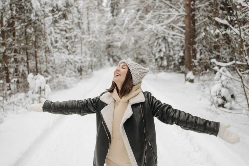 Radosna kobieta w zimowej kurtce damskiej na ścieżce w zaśnieżonym lesie