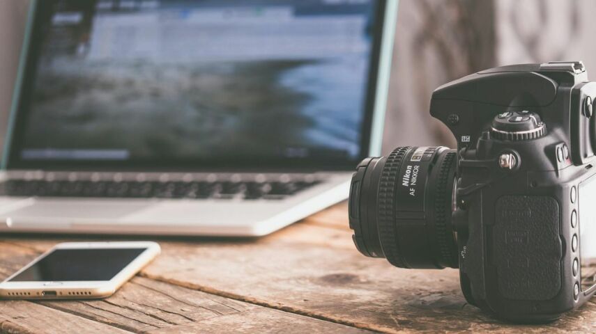 Przed otwartym laptopem aparat fotograficzny profesjonalny na biurku